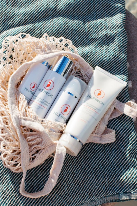 Hi, Finch mineral sunscreens in a macrame bag on striped towel beside a pool with blue water – summer skincare essentials