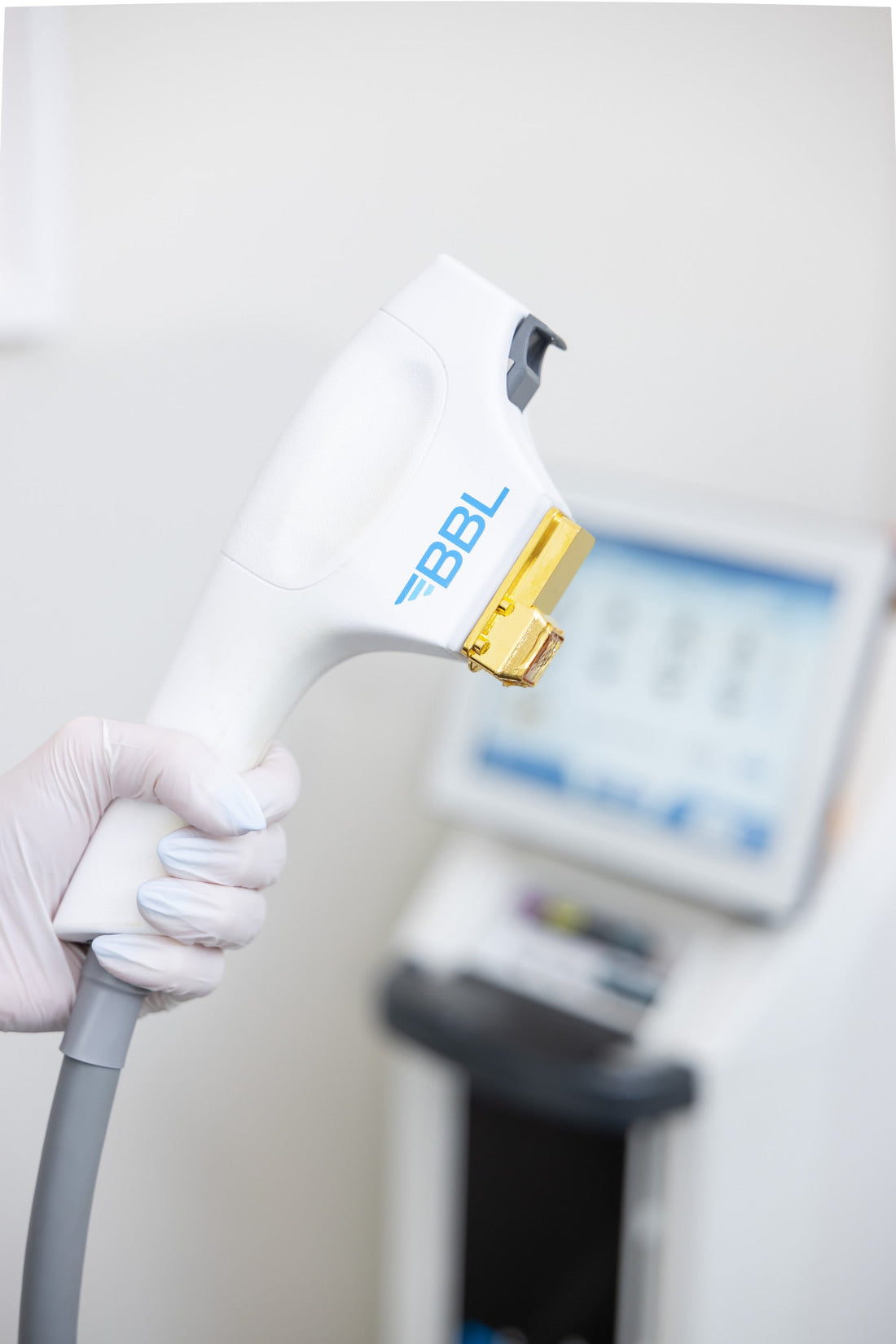 “Close-up of a gloved medical provider holding a BBL HERO handpiece in a cosmetic dermatology treatment room, with the laser device base visible in the background.”