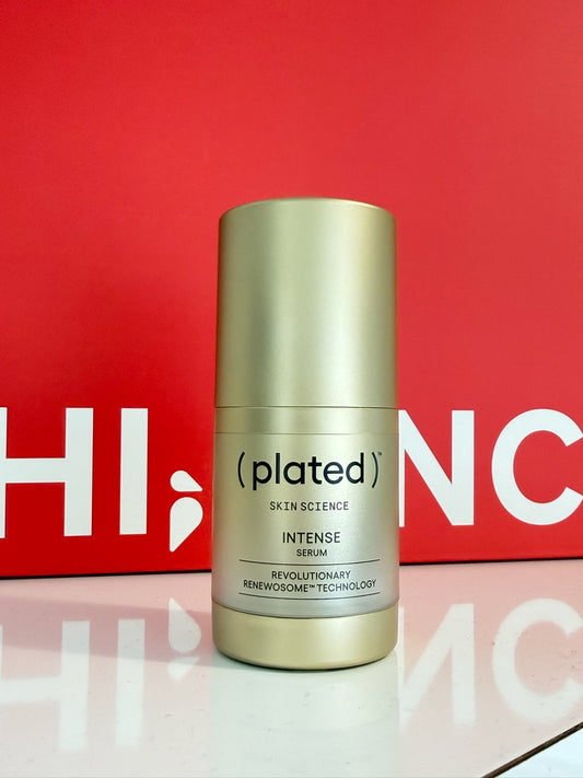 Gold cylindrical bottle of (plated)™ Skin Science Intense Serum displayed in front of the Hi, Finch red branded backdrop.