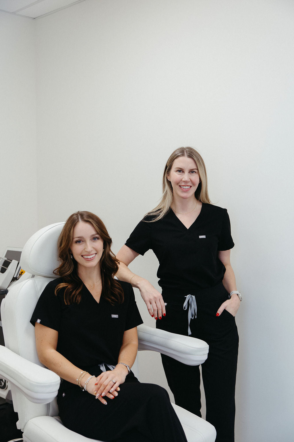 Hi, Finch nurse practitioners in a professional skincare clinic setting, smiling beside a treatment chair.