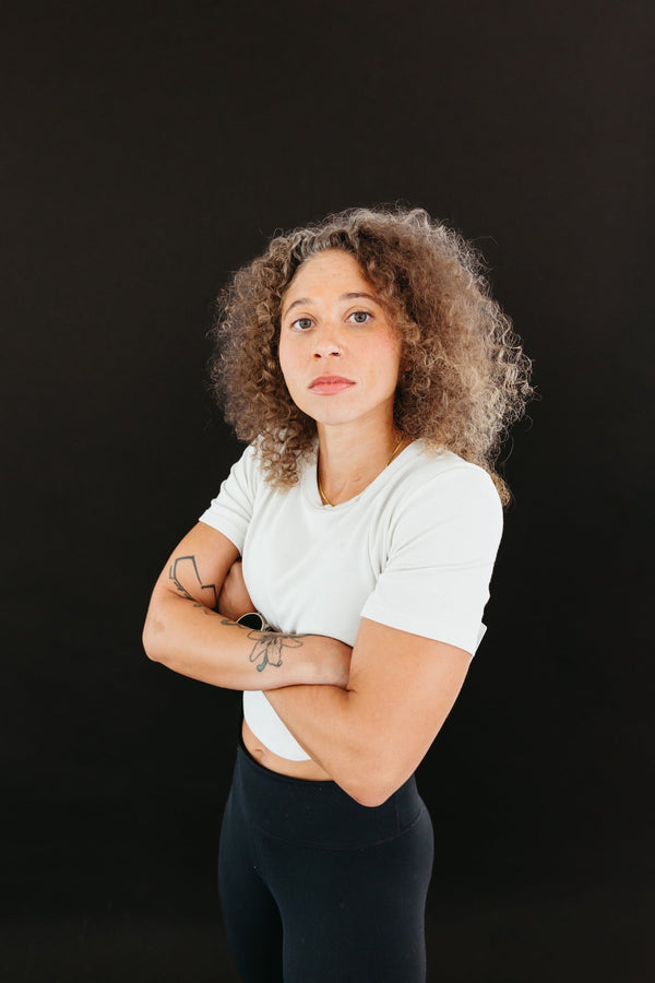 Confident woman with curly hair standing with arms crossed and looking directly at the camera.