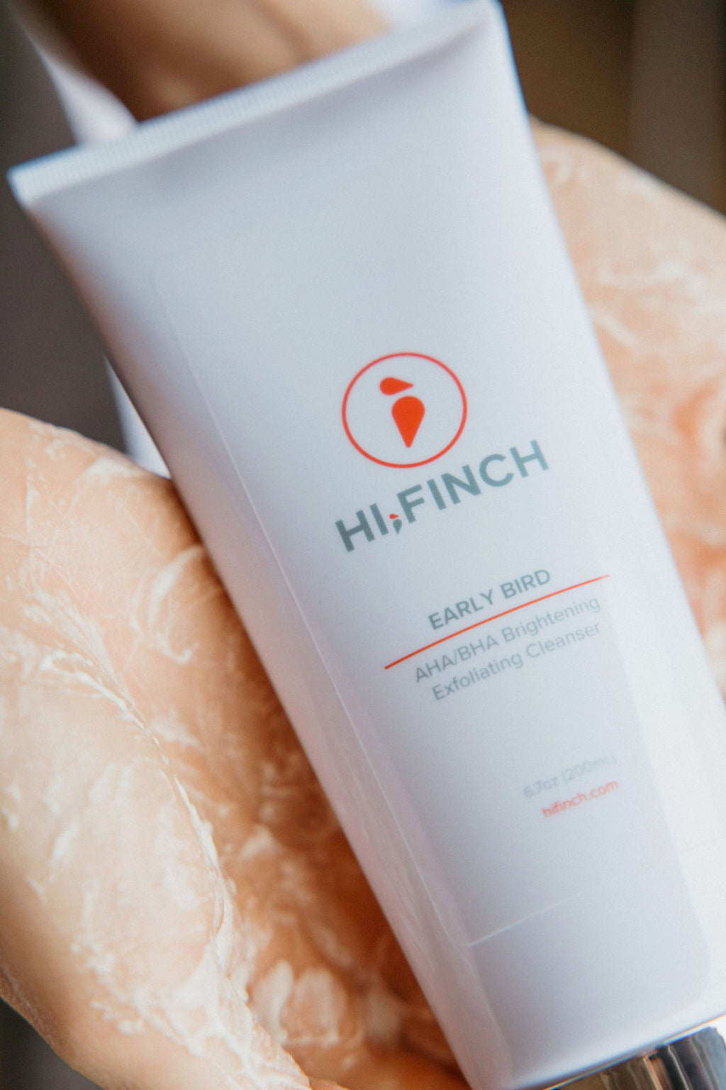 Hands holding Hi, Finch Early Bird AHA/BHA Exfoliating Cleanser, a skincare product designed to exfoliate, brighten, and promote smooth, radiant skin with the power of AHAs and BHAs.