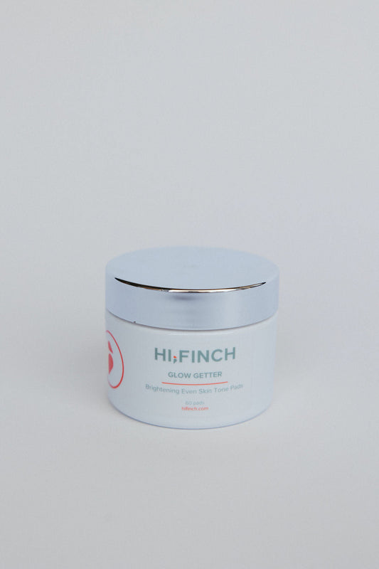 "White jar of Hi, Finch Glow Getter brightening pads with a silver lid, labeled Brightening Even Skin Tone Pads, 60 pads, against a plain light gray background."