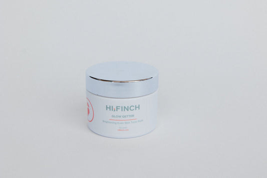 A white jar of Hi, Finch Glow Getter Brightening Even Skin Tone Pads with a silver lid, placed on a light gray background.