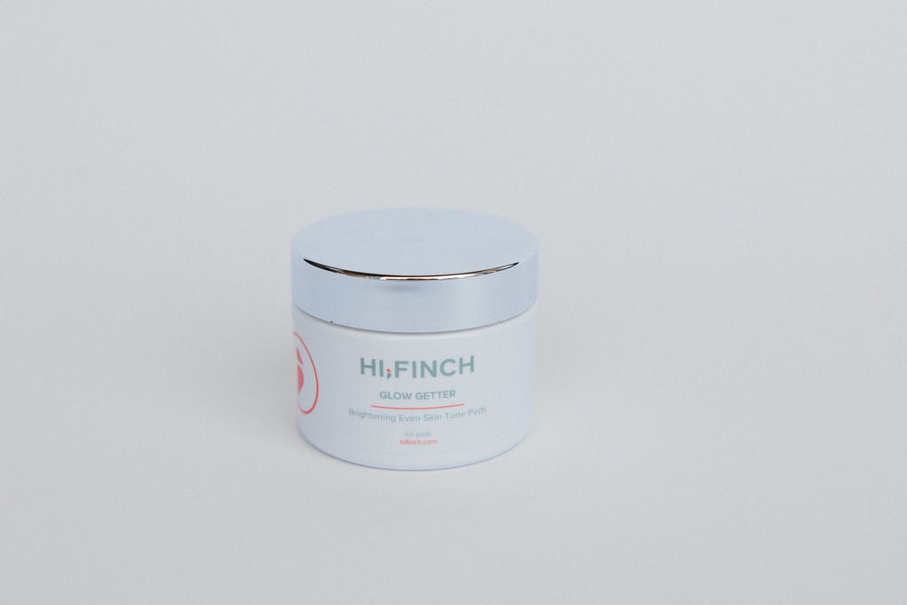 A white jar of Hi, Finch Glow Getter Brightening Even Skin Tone Pads with a silver lid, placed on a light gray background.