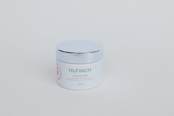 A white jar of Hi, Finch Glow Getter Brightening Even Skin Tone Pads with a silver lid, placed on a light gray background.