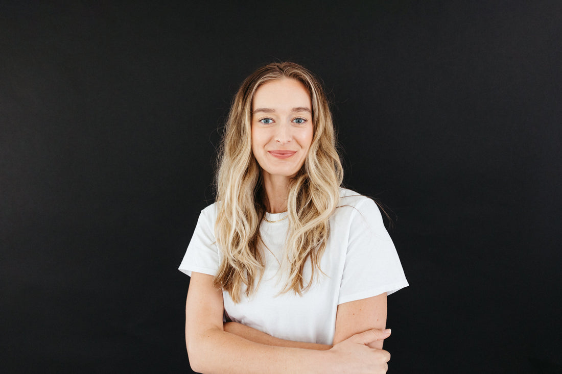 Smiling woman with long blonde hair crossing her arms, exuding confidence and healthy, glowing skin.