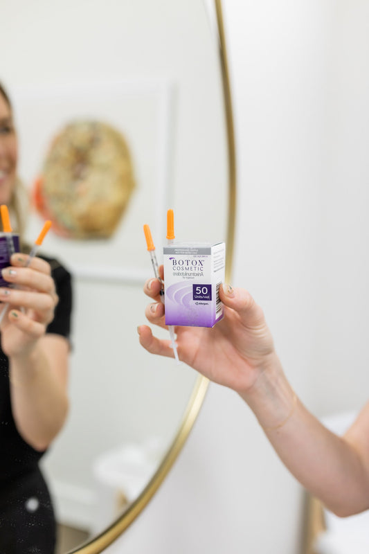 Kayli Krasnow, nurse practitioner in Nashville, holding a box of Botox and injection needles, looking in mirror at Hi, Finch Aesthetics